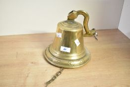 A late 20th-century brass ship-style bell, featuring a floral pattern to the rim and a hinged wall-