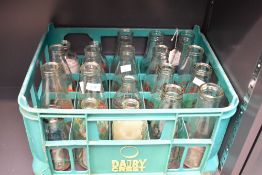 A vintage Dairy Crest plastic milk crate containing a selection of glass milk bottles by a variety
