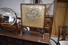 An early 20th century silkwork and mahogany fire screen, of traditional design with Chinese dragon