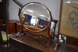 An Edwardian mahogany oval swing dressing mirror, the oval bevelled plate pivoted between shaped