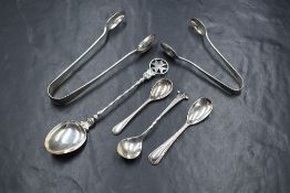 A small assortment of silver flatware, comprising two pairs of sugar tongs, three condiment spoons