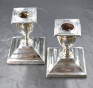 A pair of Edwardian silver candle sticks, of squat form having square sconces, raised on canted