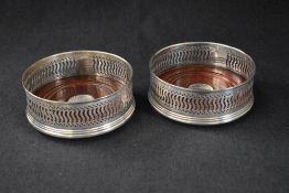 A pair of Elizabeth II silver wine coasters, having decorative pierced walls, wooden base and