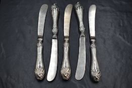 A group of five Edwardian silver handled butter knives, having decorative scroll work, marks for