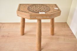 A vintage wooden milking stool, upon three turned legs, having a pyrographic geometric pattern atop,
