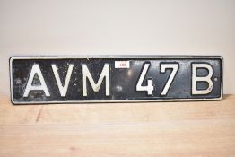 A vintage black and white aluminium number plate having raised letters and edge AVM 47B.