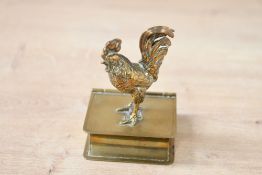 A small 20th-century brass novelty cockerel stamp holder, with the cockeral perched upon a book,