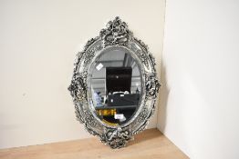 A decorative and attractive reproduction silver-effect oval bevelled wall mirror, decorated with