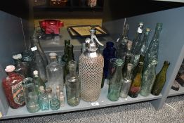 A selection of mixed antique and vintage glass bottles, including wire-bound soda siphon, coloured