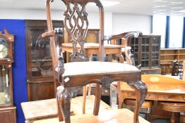 A reproduction hardwood carver chair in the Chippendale style with overstuffed seat, scrollwork arms