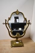 A vintage brass tilting vanity mirror, having ornate foliate detailing, upon a graduated stand,