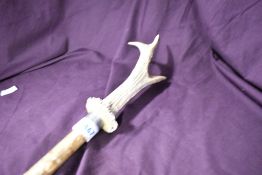 A wooden walking stick with metal feral at each end with an antler mounted on the top to form a