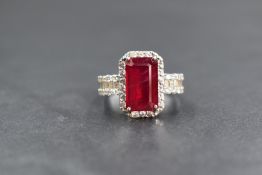 An 18ct white gold ruby and diamond set cluster ring, the central emerald cut ruby measuring