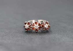 A white metal presumed gold garnet and diamond set floral ring, the three round brilliant cut