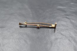 A yellow metal bar brooch modelled as a riding crop with a central red paste stone, approx 1.8g