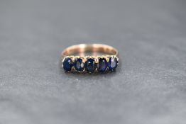 A yellow metal five stone sapphire ring in a claw set mount on a rose gold coloured loop, no marks