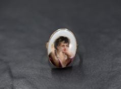 A 12ct gold portrait ring, the ceramic oval panel depicting a young gentleman in a bezel setting,