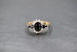 A 9ct gold sapphire and diamond set cluster ring, the central oval cut sapphire in a diamond chip