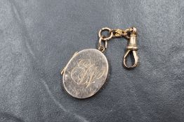 A yellow metal presumed gold locket, of oval form having 'EW' monogram, on a 9ct gold dog clip