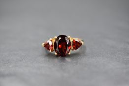 A 9ct gold garnet set trilogy ring, the central oval cut garnet flanked by a trillion cut garnet