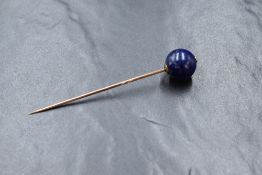 A yellow metal stick pin, presumed 9ct rose gold having a spherical lapis lazuli terminal bead,