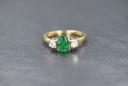 An 18ct gold emerald and diamond set three stone ring, the central oval cut emerald measuring