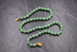 A knotted string of jade style beads of even form, having a silver gilt filigree box clasp, approx