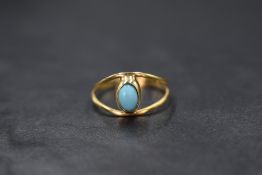 A yellow metal split loop ring stamped 18/750 having a central turquoise in a collared mount, size N