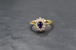 An 18ct gold sapphire and diamond cluster ring, the central oval sapphire of good colour in a raised