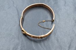 A 9ct gold hinged bangle, having a buckle motif and scroll decoration, clasp is broken and various