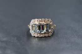 A yellow metal presumed gold aquamarine and diamond set cluster ring, the three graduated emerald