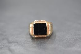 A 9ct gold onyx set signet ring, the central square onyx panel having a decorative border and