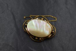 A yellow metal mother-of-pearl set brooch, the oval bezel set mother-of-pearl in a decorative