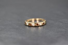 A 9ct gold half eternity ring being set with seven cubic zirconia and red paste stones on a 9ct gold