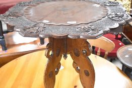 An Oriental style (believed to be Burmese) table having shaped and foliate carved top, on folding