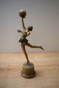 An Art Deco style bronze effect dancer figurine depicted holding a ball, raised on a circular