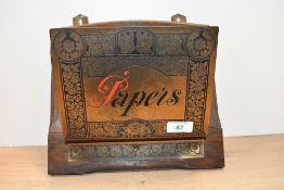 An early 20th-century brass and oak paper rack, featuring a decorative brass plating embossed with