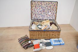 A vintage wicker sewing box, featuring floral fabric lining and a selection of sewing notions,
