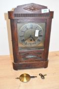 An early 20th-century wooden wall clock, featuring a decorative carved top and a glass-panelled
