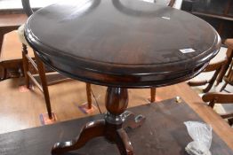 A reproduction dark stained pedestal table having circular top on turned column and triple splay