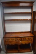 A reproduction yew wood dresser having open delft rack over three drawer base with shelf under,