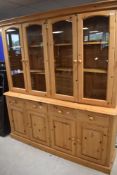 A modern pine bookcase comprising glazed section over four drawers and two double cupboards, width