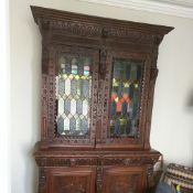 A 19th Century carved oak bookcase, having stained glass doors to the bookcase section and lion mask