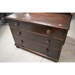A Victorian dark stained pine chest of three long drawers, having shaped ledge back and turned