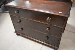 A Victorian dark stained pine chest of three long drawers, having shaped ledge back and turned