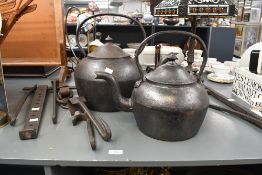 Two large Victorian cast iron kettles, featuring a prominent finial, domed lid and curved spout;