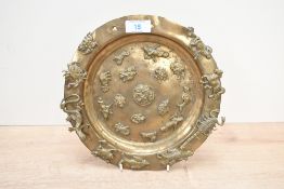A 20th-century Tibetan-style brass plate, featuring applied figures of animals and deities to both