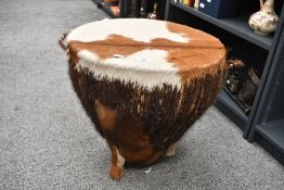 A large late 20th-century African drum-formed side table, covered in brown and white cowhide, upon