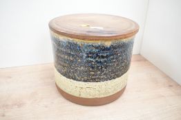 A large contemporary studio pottery container, having a turned wooden lid and two tone drip glaze