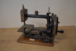 An antique So-All sewing machine, black painted cast iron on a wood base, floral decoration.
